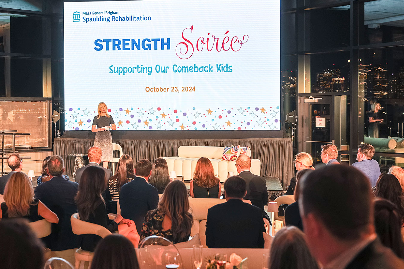 An audience of well-dressed people watches a presentation.