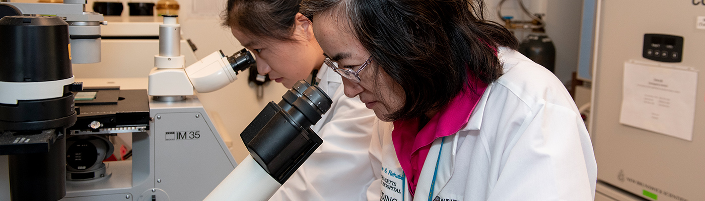 Two researchers in a lab peering into microscopes.