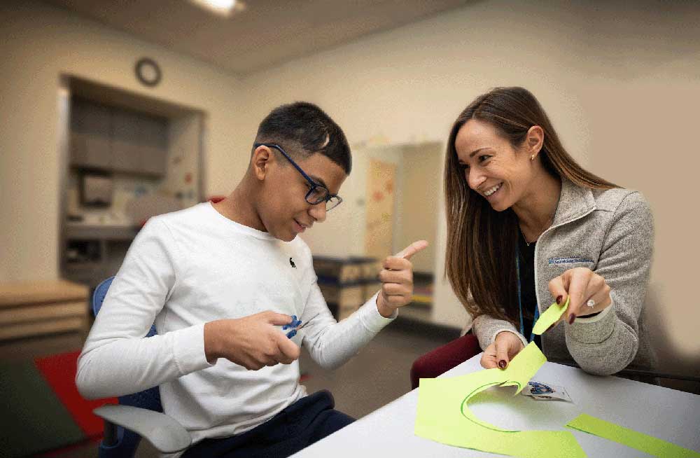 A young man cuts circles out of construction paper to practice skills with his occupational therapist.