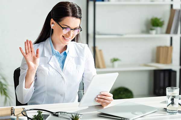 A smiling female doctor reads a tablet at her desk.