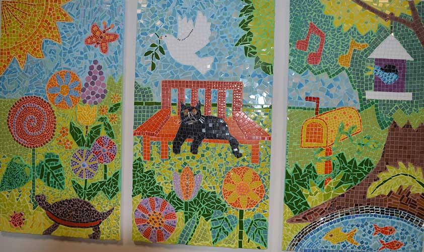 A three-panel mosaic. The left panel shows the sun shining on a profusion of brightly colored flowers. The center panel shows a black cat lounging on a garden bench, and a dove flying above with an olive sprig in its beak. The right panel shows a birdhouse hanging fron a lush tree, and a blue bird singing in the doorway. Under the tree is a bright orange mailbox surrounded by greenery.