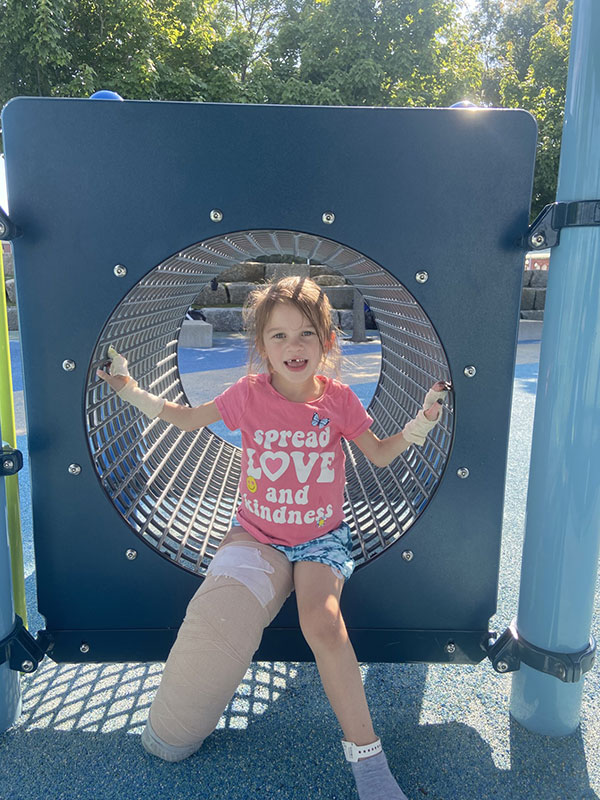 Addie, a 7-year-old with her right leg in heavy bandages, plays in a tunnel at a playground.