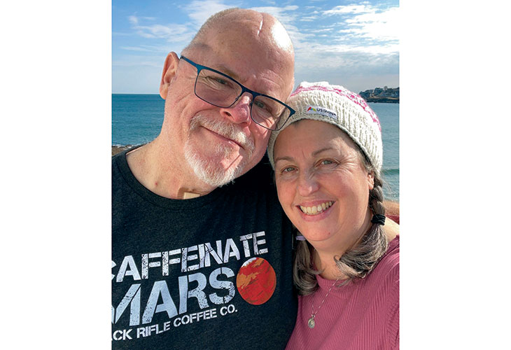 Doug and Laura, an older white couple, side-hugging with the sea in the background.