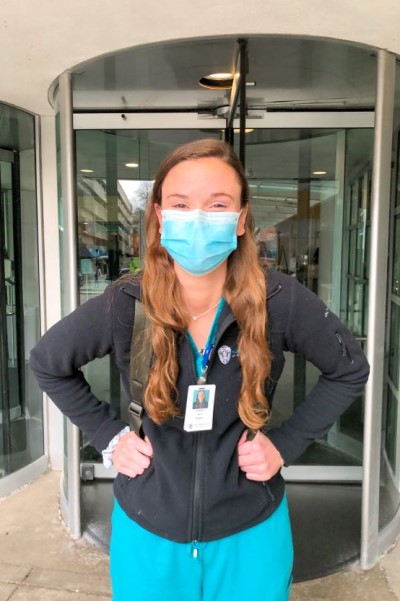 Sarah in scrubs and a backpack in front of a medical building.