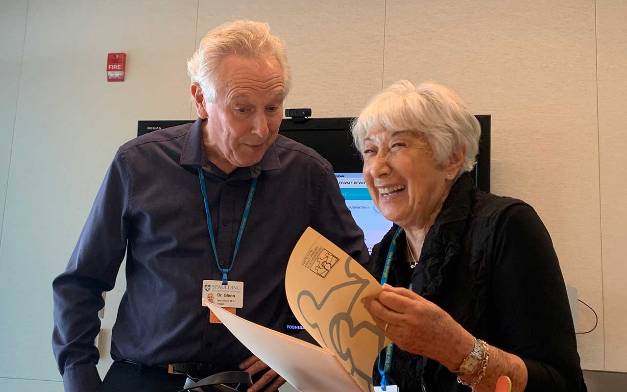 Mel Glenn and Marilyn Spivack laughing over an open booklet.